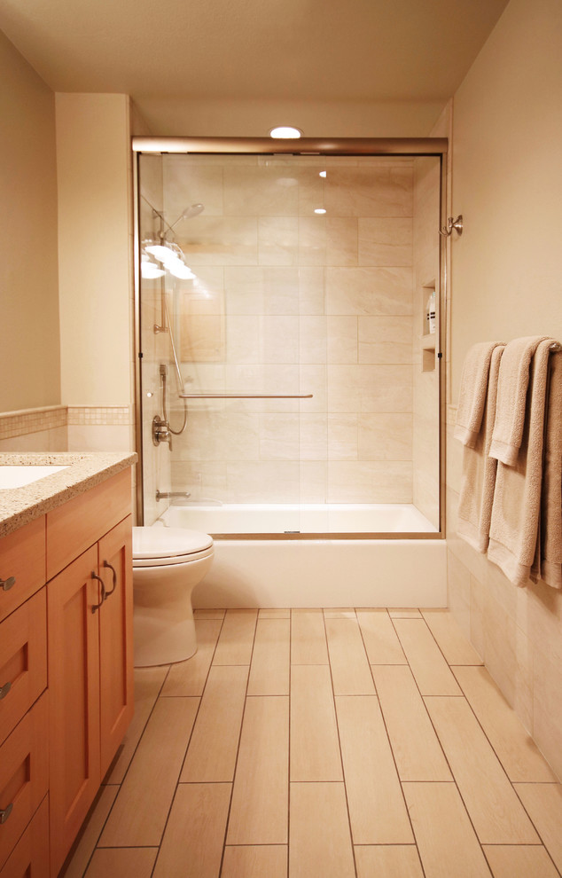Cette image montre une salle d'eau traditionnelle en bois clair de taille moyenne avec un placard à porte shaker, une baignoire en alcôve, un combiné douche/baignoire, WC à poser, un carrelage beige, des carreaux de porcelaine, un mur beige, parquet clair, un lavabo encastré et un plan de toilette en granite.