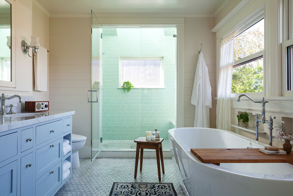 На фото: главная ванная комната в классическом стиле с синими фасадами, отдельно стоящей ванной, душем в нише, зеленой плиткой, плиткой кабанчик, бежевыми стенами, мраморным полом, врезной раковиной, мраморной столешницей, серым полом, душем с распашными дверями, серой столешницей и окном