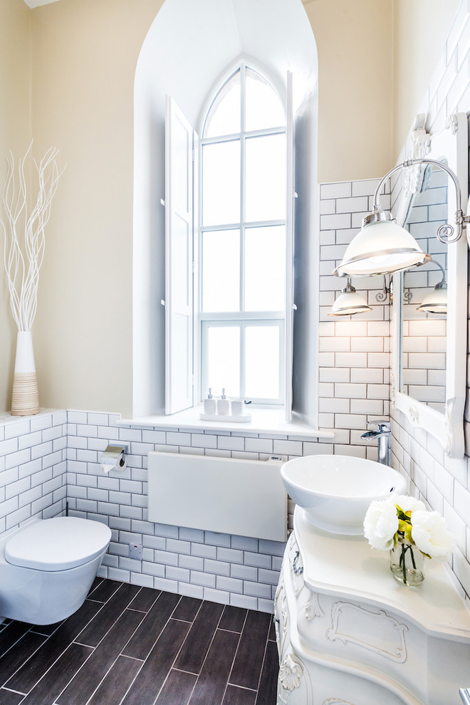 Aménagement d'une salle de bain classique avec des portes de placard blanches, WC suspendus, un carrelage blanc, un carrelage métro, un mur beige, une vasque et un placard avec porte à panneau surélevé.