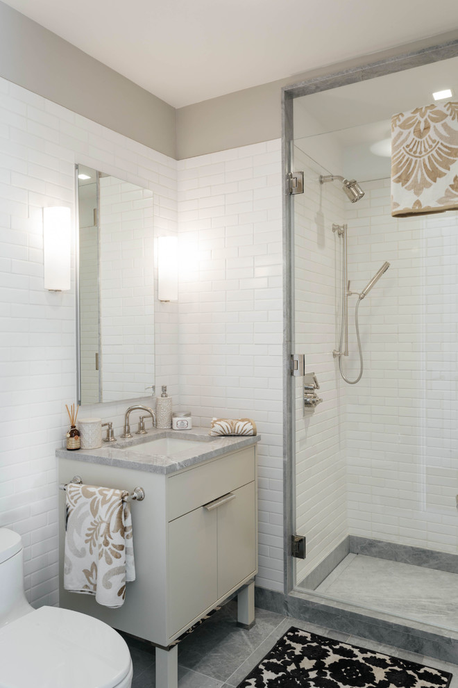 Inredning av ett modernt mellanstort badrum med dusch, med släta luckor, grå skåp, en toalettstol med hel cisternkåpa, vit kakel, tunnelbanekakel, grå väggar, ett undermonterad handfat, marmorbänkskiva och en hörndusch