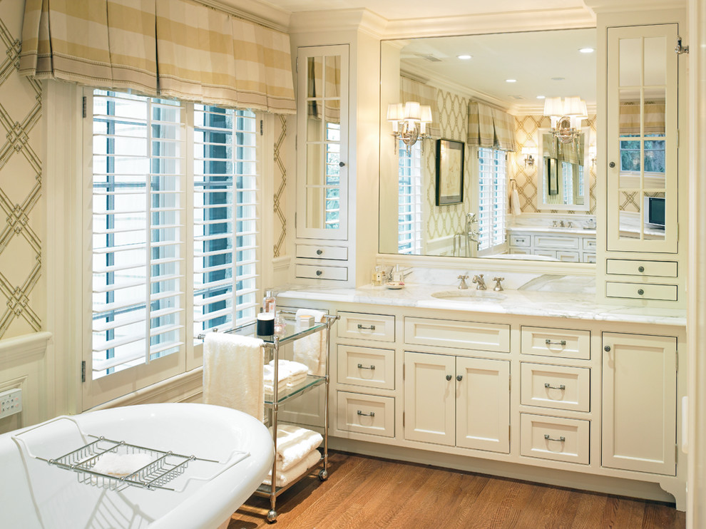 Idéer för ett mellanstort klassiskt en-suite badrum, med ett fristående badkar, ett undermonterad handfat, vita skåp, marmorbänkskiva, vita väggar, mellanmörkt trägolv och luckor med infälld panel