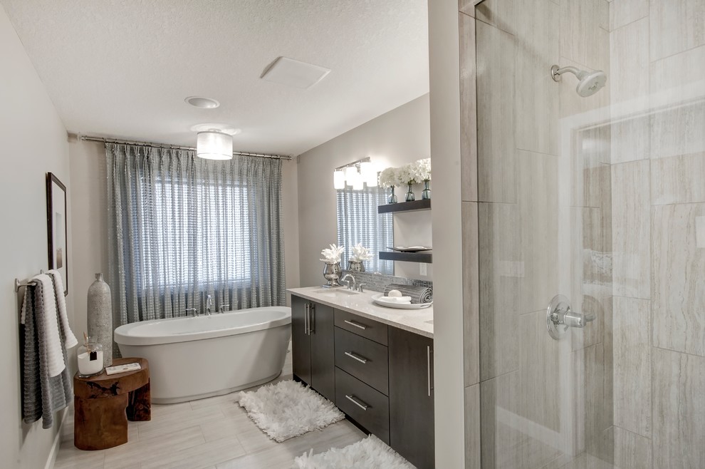 Modelo de cuarto de baño actual con puertas de armario de madera en tonos medios, bañera exenta, suelo de madera clara, armarios con paneles lisos y encimera de cuarcita