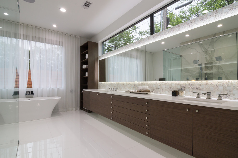 Photo of a large contemporary ensuite bathroom in Dallas with flat-panel cabinets, dark wood cabinets, a freestanding bath, a built-in shower, a one-piece toilet, white tiles, glass tiles, white walls, porcelain flooring, a built-in sink and engineered stone worktops.