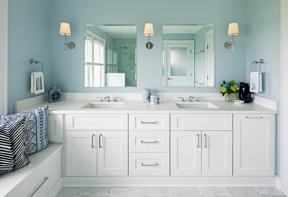Modelo de cuarto de baño principal marinero con armarios estilo shaker, puertas de armario blancas, paredes azules, lavabo bajoencimera, suelo gris, encimeras blancas y espejo con luz