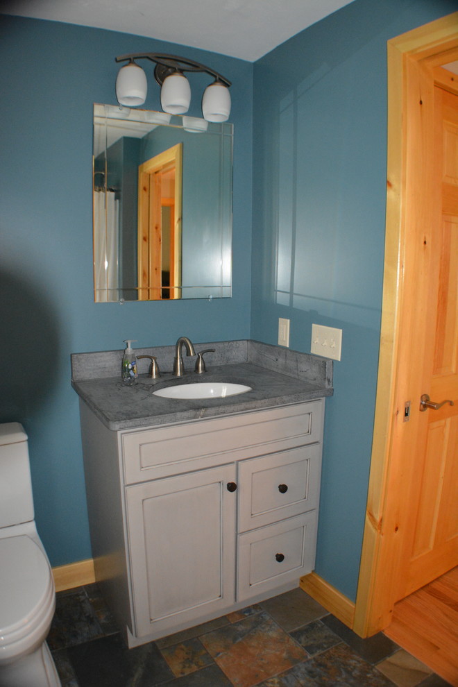 Design ideas for a small traditional family bathroom in Boston with flat-panel cabinets, distressed cabinets, a shower/bath combination, a two-piece toilet, cement tiles, blue walls, porcelain flooring, a submerged sink, soapstone worktops, multi-coloured tiles and an alcove bath.