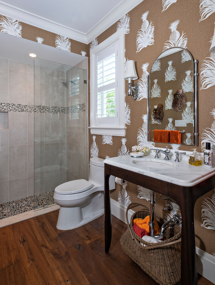 Duschbad mit offenen Schränken, Duschnische, Wandtoilette mit Spülkasten, beigen Fliesen, brauner Wandfarbe, dunklem Holzboden, Waschtischkonsole, braunem Boden und weißer Waschtischplatte in Miami