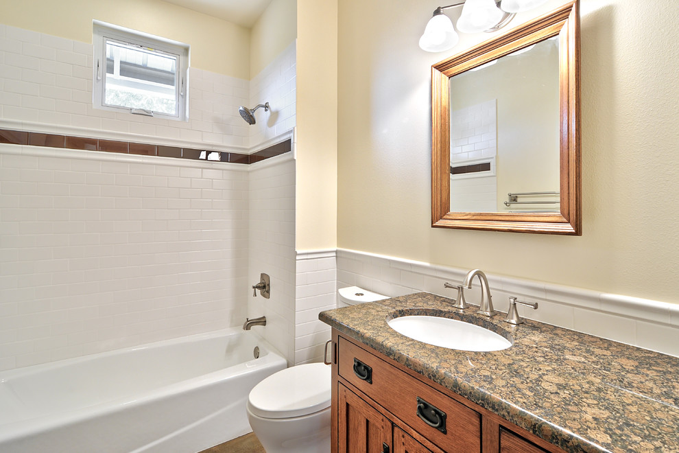 Immagine di una stanza da bagno american style con lavabo sottopiano, vasca ad alcova, consolle stile comò, top in granito, piastrelle bianche, piastrelle in ceramica e ante in legno scuro
