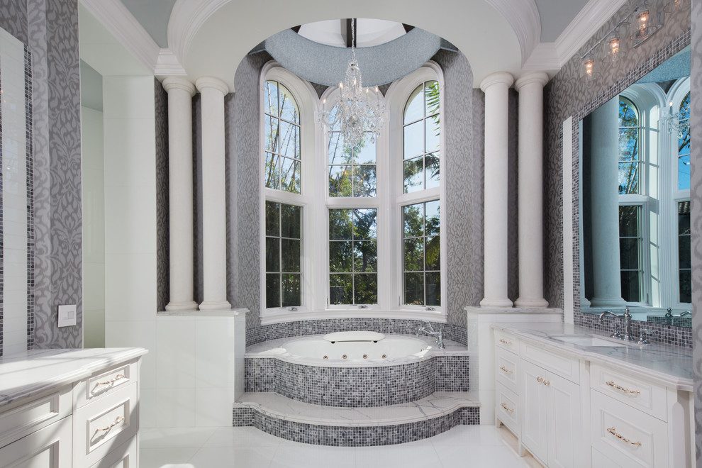 Cette photo montre une salle de bain principale chic avec un placard avec porte à panneau encastré, des portes de placard blanches, une baignoire encastrée, un carrelage multicolore, mosaïque, un mur gris, un lavabo encastré, un sol blanc et un plan de toilette blanc.