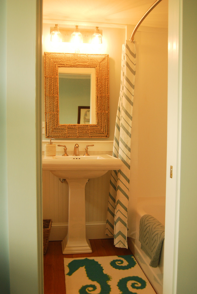 Foto de cuarto de baño marinero con combinación de ducha y bañera, lavabo con pedestal, bañera empotrada, paredes azules y suelo de madera en tonos medios