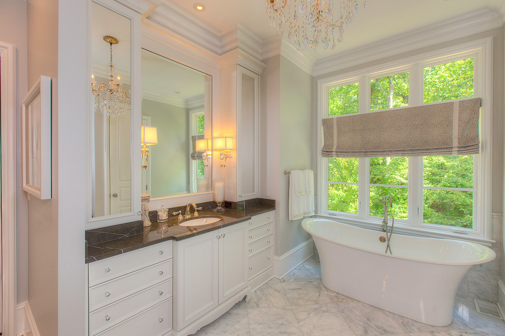 Modelo de cuarto de baño tradicional con suelo de mármol, lavabo bajoencimera, armarios con paneles empotrados, puertas de armario blancas y bañera exenta