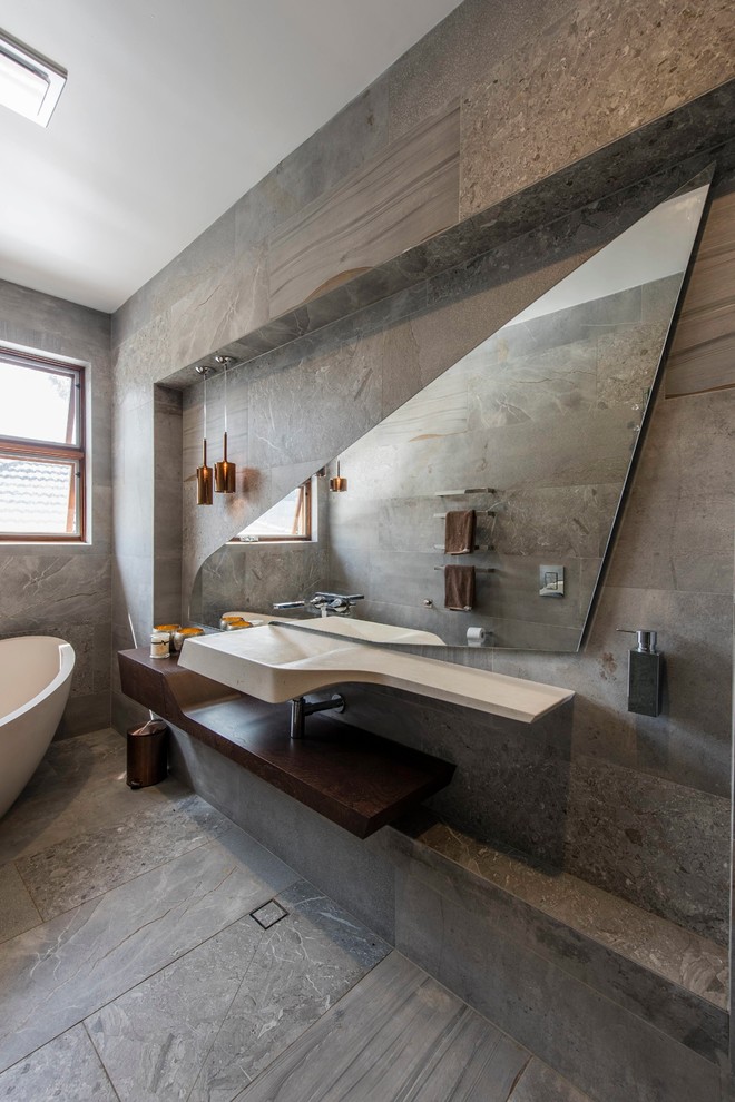 Ejemplo de cuarto de baño principal costero con armarios abiertos, bañera exenta, sanitario de pared, baldosas y/o azulejos grises, paredes grises, lavabo integrado y suelo gris