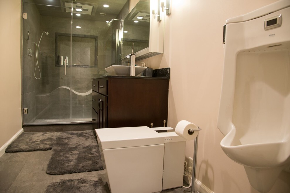 Idées déco pour une grande salle de bain contemporaine en bois foncé avec un placard à porte plane, un urinoir, un carrelage gris, un carrelage de pierre, un mur beige, carreaux de ciment au sol, une vasque, un plan de toilette en granite, un sol beige, une cabine de douche à porte battante et un plan de toilette noir.