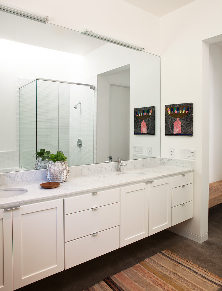 Cette image montre une salle de bain principale rustique de taille moyenne avec un lavabo encastré, un placard à porte shaker, des portes de placard blanches, une douche d'angle, sol en béton ciré, un mur blanc, un plan de toilette en marbre et un plan de toilette gris.
