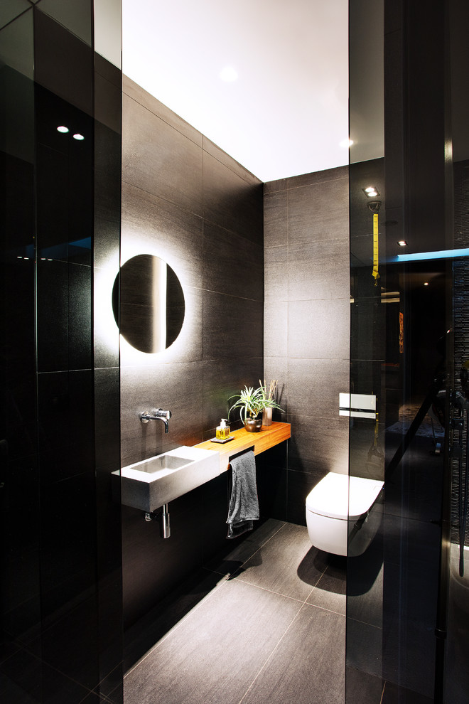 Modernes Duschbad mit Wandtoilette, grauen Fliesen, grauer Wandfarbe, Wandwaschbecken, Waschtisch aus Holz, grauem Boden und brauner Waschtischplatte in London