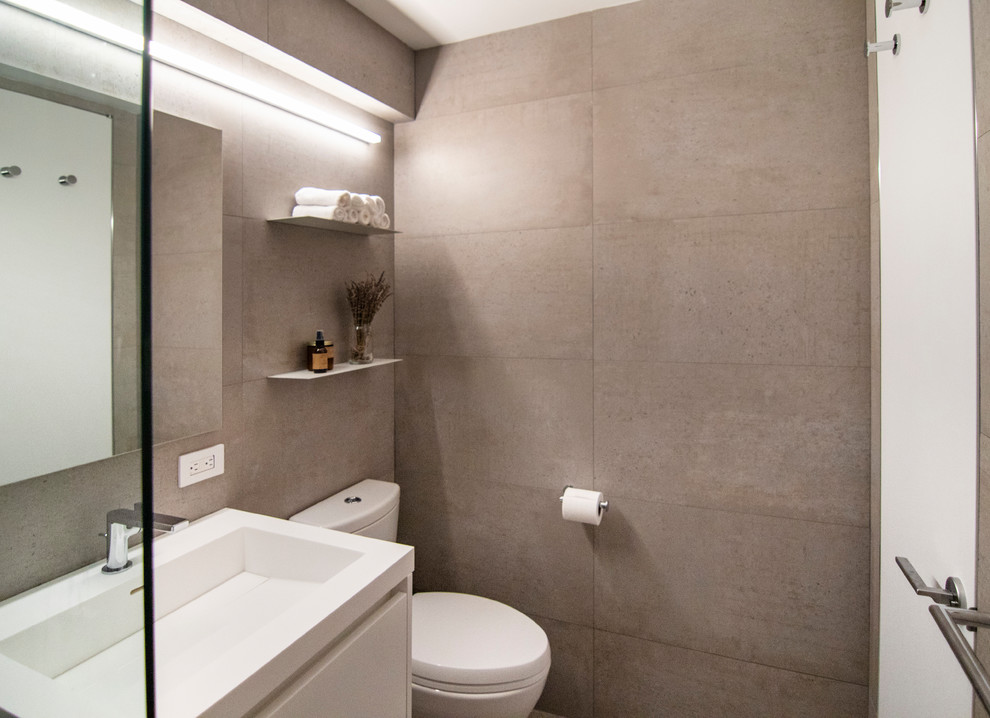 Modern inredning av ett litet vit vitt en-suite badrum, med släta luckor, vita skåp, ett platsbyggt badkar, en dusch/badkar-kombination, en toalettstol med hel cisternkåpa, grå kakel, porslinskakel, grå väggar, klinkergolv i porslin, ett integrerad handfat, bänkskiva i akrylsten, grått golv och med dusch som är öppen