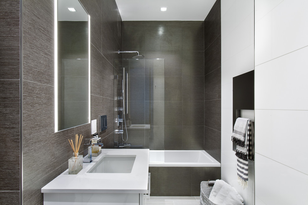 Modern inredning av ett litet badrum med dusch, med släta luckor, vita skåp, ett badkar i en alkov, en dusch/badkar-kombination, grå kakel, porslinskakel, vita väggar, klinkergolv i porslin, ett undermonterad handfat och bänkskiva i akrylsten