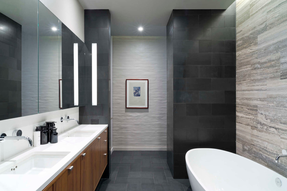 Modernes Badezimmer mit Unterbauwaschbecken, flächenbündigen Schrankfronten, hellbraunen Holzschränken, freistehender Badewanne und schwarzen Fliesen in New York