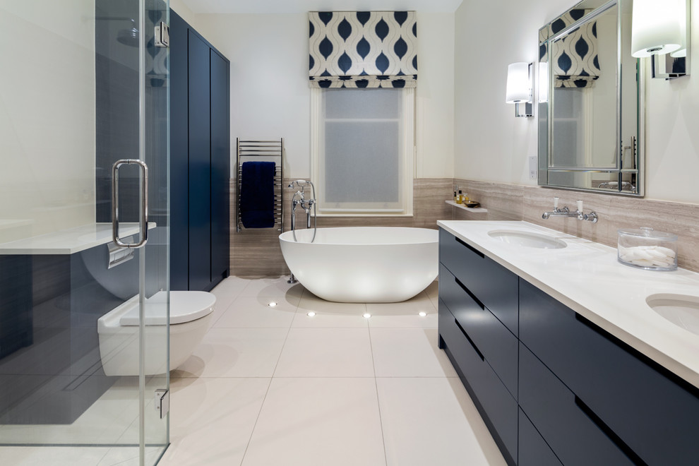 Modern inredning av ett en-suite badrum, med släta luckor, blå skåp, ett fristående badkar, en hörndusch, en vägghängd toalettstol, vita väggar, ett undermonterad handfat, vitt golv och dusch med gångjärnsdörr