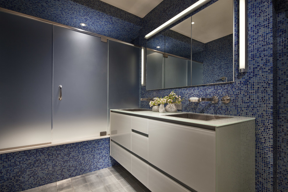 Imagen de cuarto de baño principal contemporáneo de tamaño medio con lavabo encastrado, armarios con paneles lisos, puertas de armario blancas, encimera de vidrio, bañera empotrada, baldosas y/o azulejos azules y baldosas y/o azulejos en mosaico