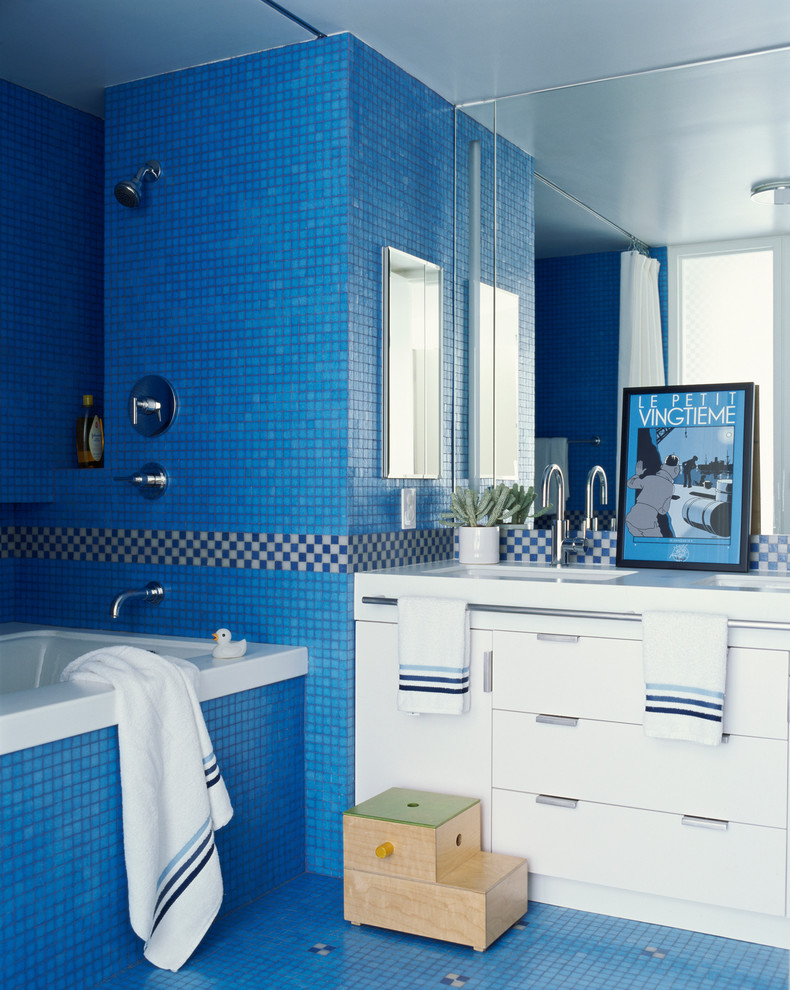 ニューヨークにあるお手頃価格の中くらいなコンテンポラリースタイルのおしゃれな子供用バスルーム (フラットパネル扉のキャビネット、白いキャビネット、人工大理石カウンター、ドロップイン型浴槽、シャワー付き浴槽	、青いタイル、モザイクタイル、青い壁、モザイクタイル) の写真