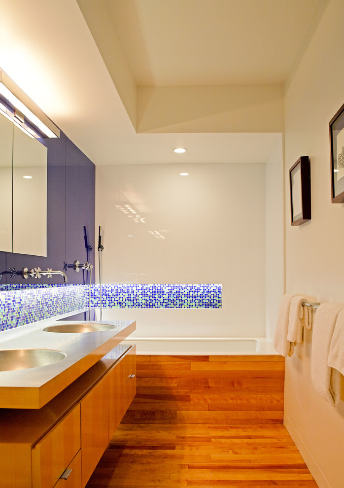 Idées déco pour une salle de bain principale contemporaine en bois clair de taille moyenne avec un lavabo intégré, un placard à porte plane, un plan de toilette en acier inoxydable, une baignoire en alcôve, un carrelage bleu, un carrelage en pâte de verre, un mur blanc et parquet clair.