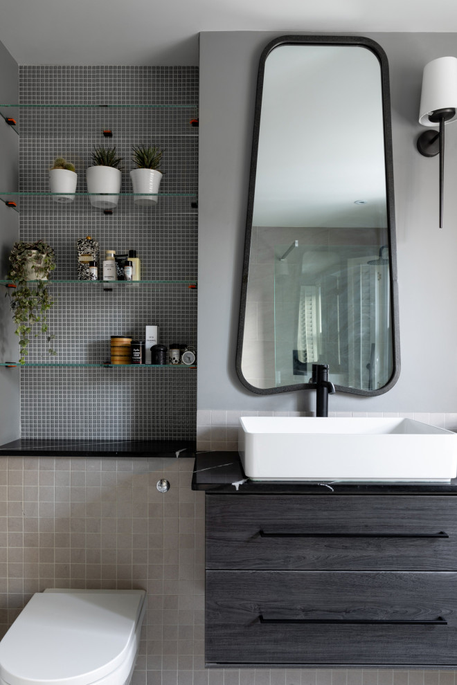 Medium sized traditional ensuite bathroom in Sussex with flat-panel cabinets, grey cabinets, a walk-in shower, a wall mounted toilet, grey tiles, porcelain tiles, grey walls, ceramic flooring, a console sink, marble worktops, grey floors, black worktops, double sinks and a floating vanity unit.