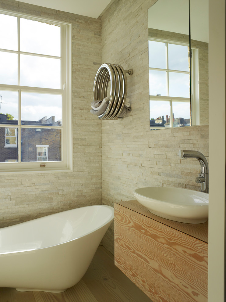 This is an example of a medium sized contemporary ensuite bathroom in London with flat-panel cabinets, light wood cabinets, a freestanding bath, a shower/bath combination, a wall mounted toilet, beige tiles, ceramic tiles, beige walls, light hardwood flooring, a vessel sink, wooden worktops, beige floors and brown worktops.