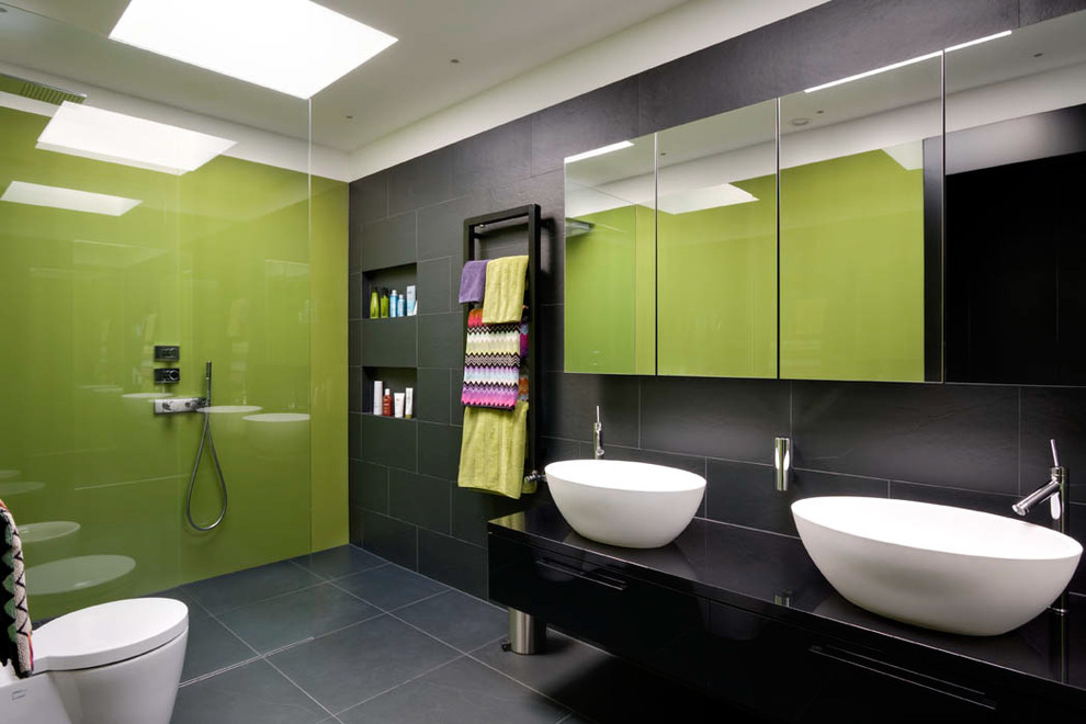 Inredning av ett modernt stort svart svart en-suite badrum, med ett fristående handfat, svarta skåp, en öppen dusch, med dusch som är öppen, släta luckor, en vägghängd toalettstol, grå kakel, skifferkakel, gröna väggar, skiffergolv, bänkskiva i akrylsten och grått golv