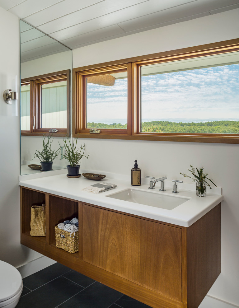 Modelo de cuarto de baño marinero con puertas de armario de madera oscura, paredes blancas, suelo negro y encimeras blancas