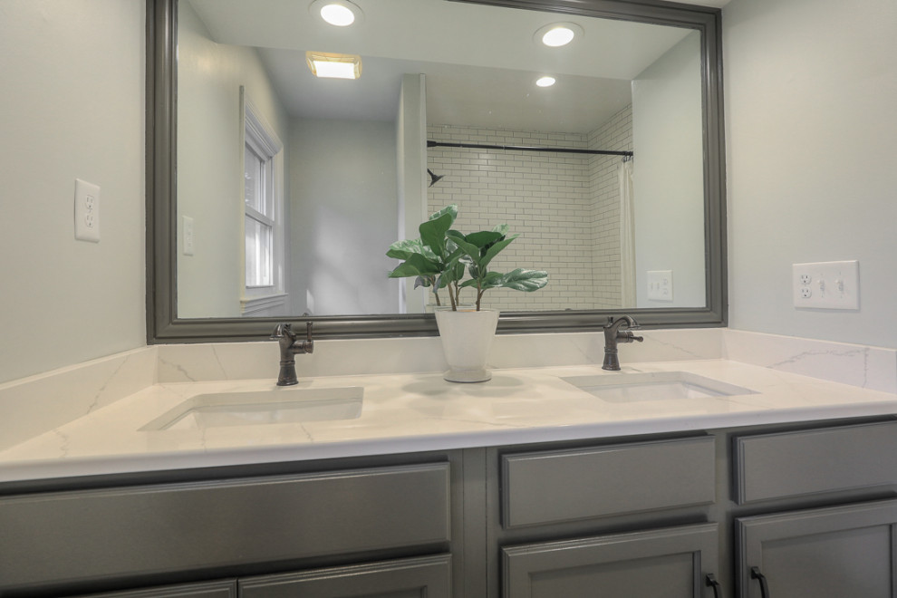 Klassisk inredning av ett vit vitt badrum, med grå skåp, en dusch/badkar-kombination, vit kakel, porslinskakel, grå väggar, klinkergolv i porslin, bänkskiva i kvarts och grått golv