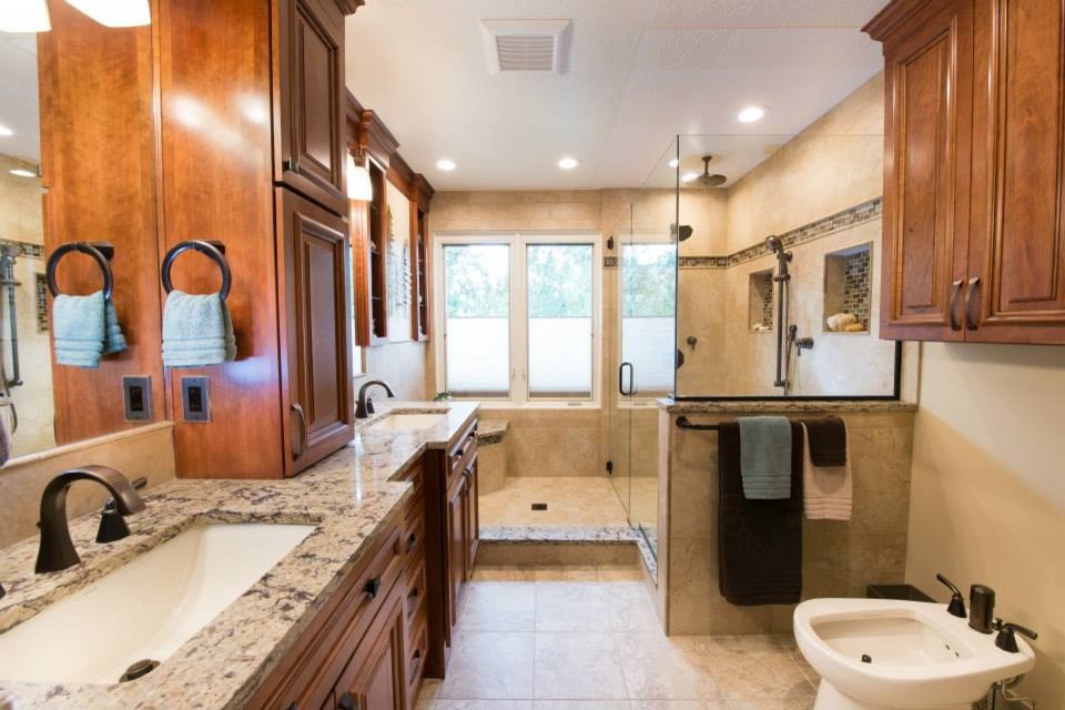Corner shower - large transitional master beige tile and porcelain tile porcelain tile and beige floor corner shower idea in Other with raised-panel cabinets, medium tone wood cabinets, a bidet, beige walls, an undermount sink, granite countertops and a hinged shower door