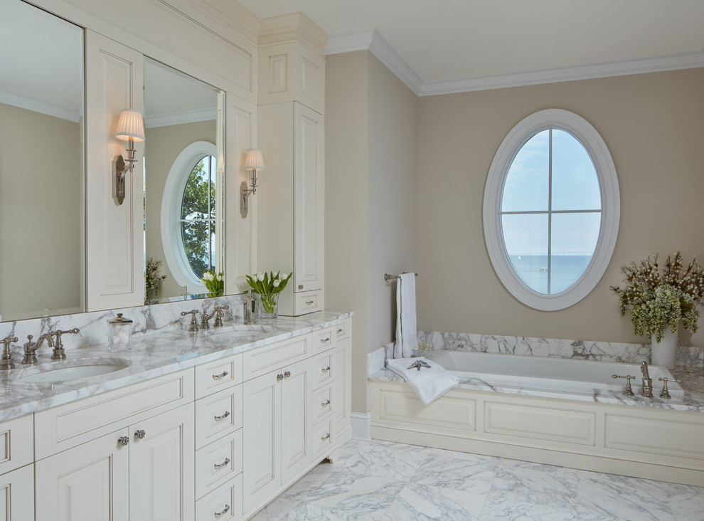Imagen de cuarto de baño principal costero con puertas de armario beige, bañera encastrada, paredes beige, lavabo bajoencimera y espejo con luz
