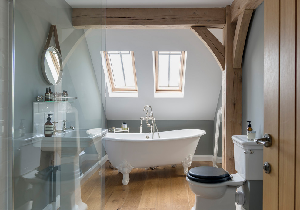 Inspiration for a country shower room bathroom in West Midlands with a claw-foot bath, a two-piece toilet, grey walls, medium hardwood flooring, a pedestal sink and brown floors.
