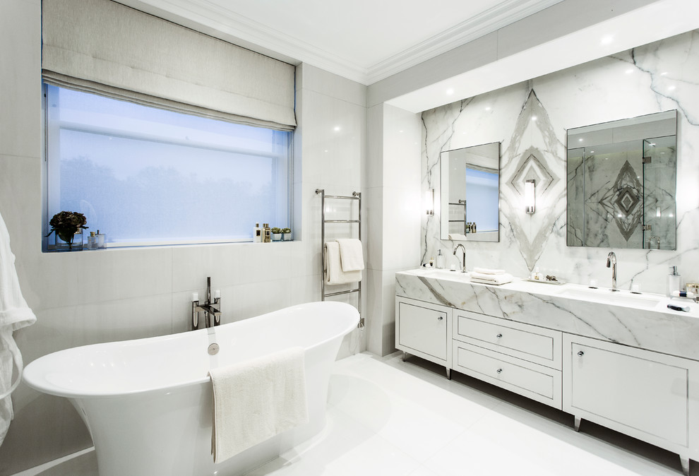 This is an example of a contemporary ensuite bathroom in London with flat-panel cabinets, white cabinets, a freestanding bath, an integrated sink and marble worktops.