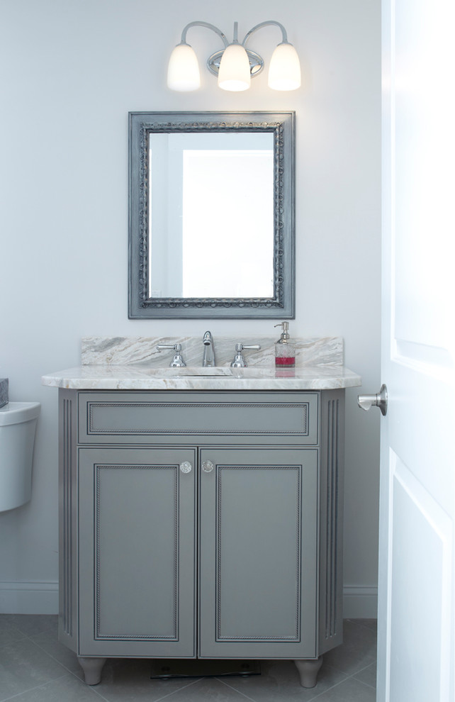 Cette photo montre une salle de bain chic de taille moyenne avec un placard à porte affleurante, des portes de placard grises, un mur blanc, un sol en carrelage de porcelaine, un lavabo encastré et un plan de toilette en marbre.