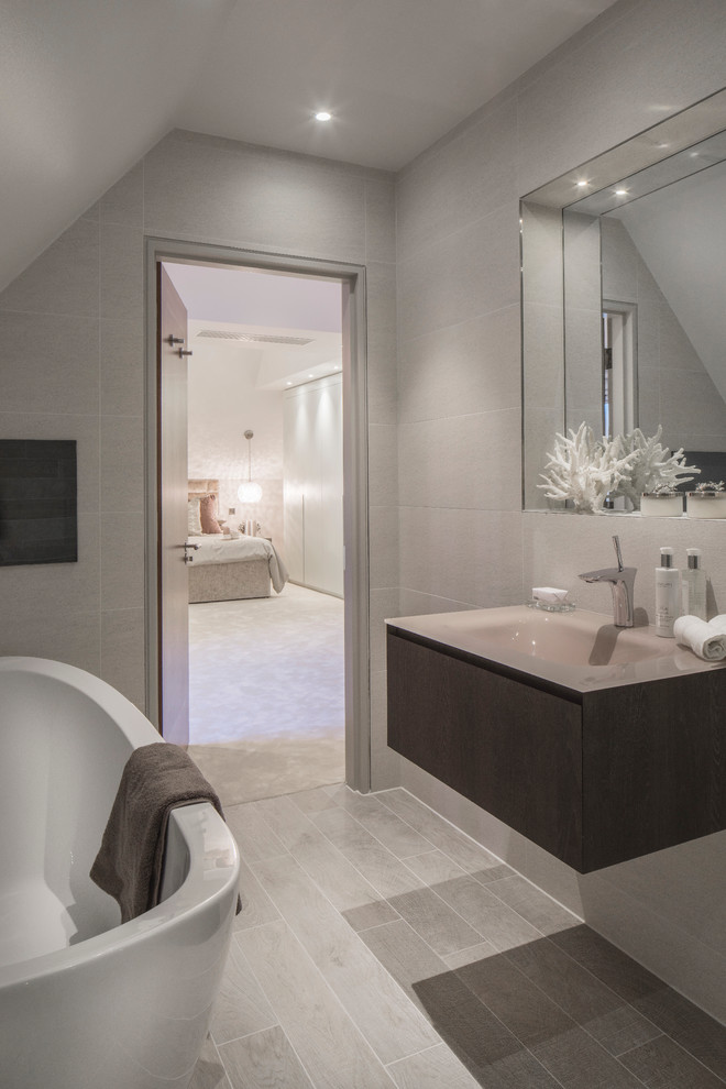 Small contemporary bathroom in London with an integrated sink, grey cabinets, glass worktops, a freestanding bath, an alcove shower, a wall mounted toilet, grey tiles, ceramic tiles, grey walls and ceramic flooring.