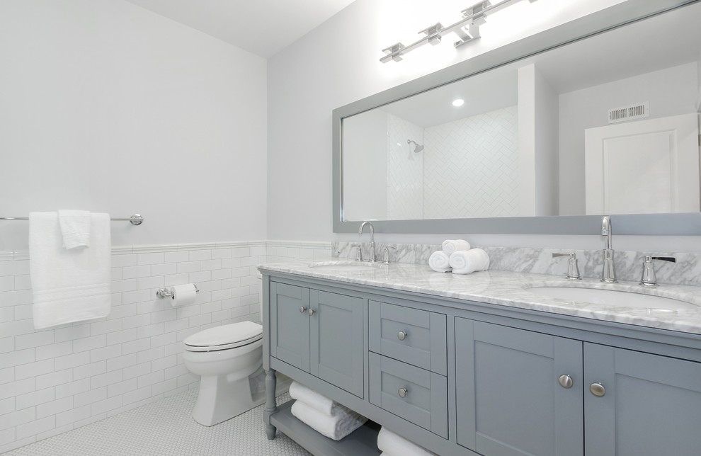 На фото: ванная комната среднего размера в стиле неоклассика (современная классика) с серыми фасадами, ванной в нише, душем над ванной, унитазом-моноблоком, белой плиткой, плиткой кабанчик, серыми стенами, полом из керамогранита, врезной раковиной, мраморной столешницей и фасадами в стиле шейкер с