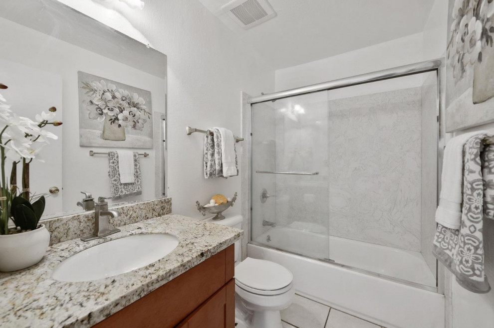 Modern inredning av ett litet brun brunt badrum med dusch, med skåp i shakerstil, skåp i mellenmörkt trä, ett badkar i en alkov, en toalettstol med hel cisternkåpa, vita väggar, klinkergolv i keramik, ett undermonterad handfat, granitbänkskiva, beiget golv och dusch med skjutdörr