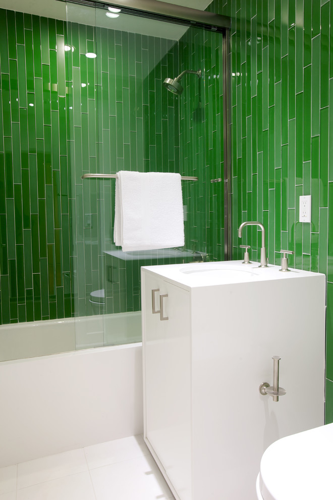 Exemple d'une salle d'eau moderne de taille moyenne avec un placard à porte plane, des portes de placard blanches, une baignoire en alcôve, un combiné douche/baignoire, un carrelage vert, un carrelage en pâte de verre, un mur vert, un sol en carrelage de porcelaine, un lavabo encastré, un plan de toilette en surface solide, un sol blanc et une cabine de douche à porte coulissante.