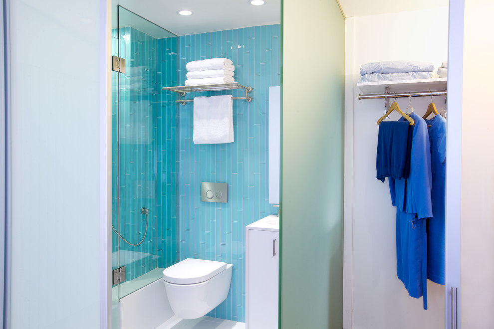 Exemple d'une salle d'eau moderne de taille moyenne avec un placard à porte plane, des portes de placard blanches, une baignoire en alcôve, un combiné douche/baignoire, WC suspendus, un carrelage bleu, un carrelage en pâte de verre, un mur bleu, un sol en carrelage de porcelaine, un sol bleu et une cabine de douche à porte battante.