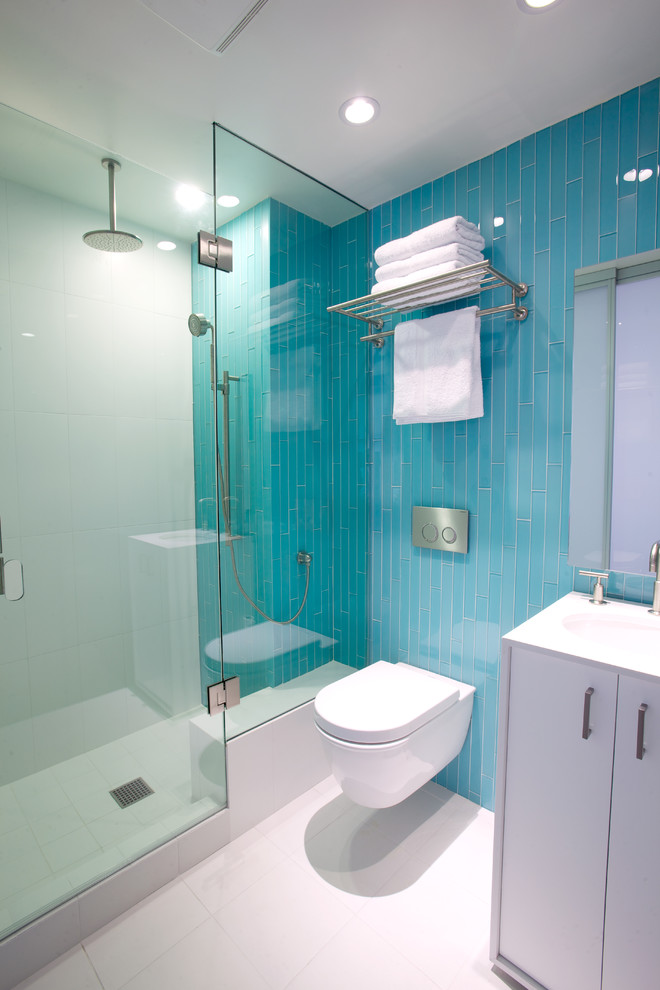 This is an example of a medium sized contemporary shower room bathroom in Los Angeles with blue tiles, flat-panel cabinets, white cabinets, an alcove shower, a wall mounted toilet, glass tiles, porcelain flooring, a submerged sink, white floors, a hinged door and a feature wall.