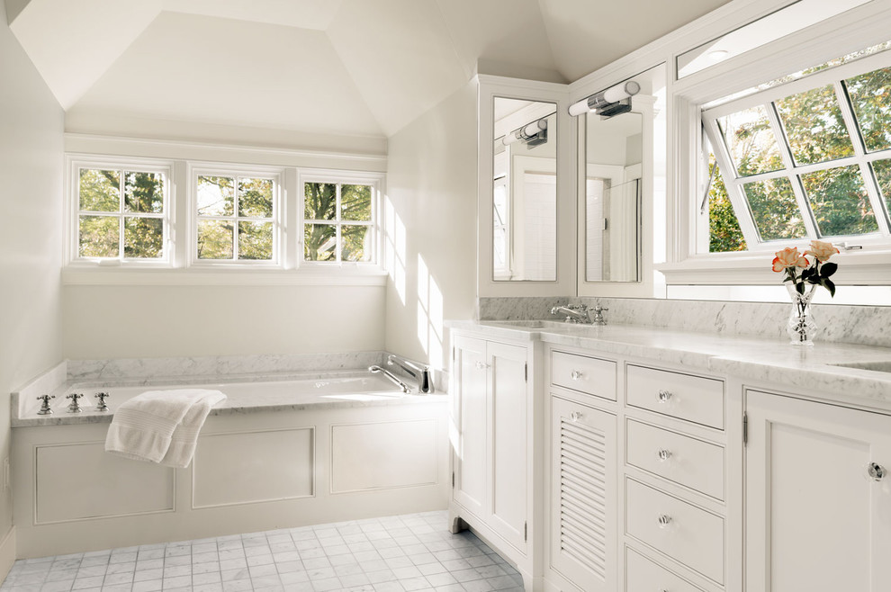 Пример оригинального дизайна: главная ванная комната в классическом стиле с врезной раковиной, белыми фасадами, мраморной столешницей, полновстраиваемой ванной, белой плиткой, каменной плиткой, белыми стенами, мраморным полом, фасадами с утопленной филенкой, белой столешницей и окном