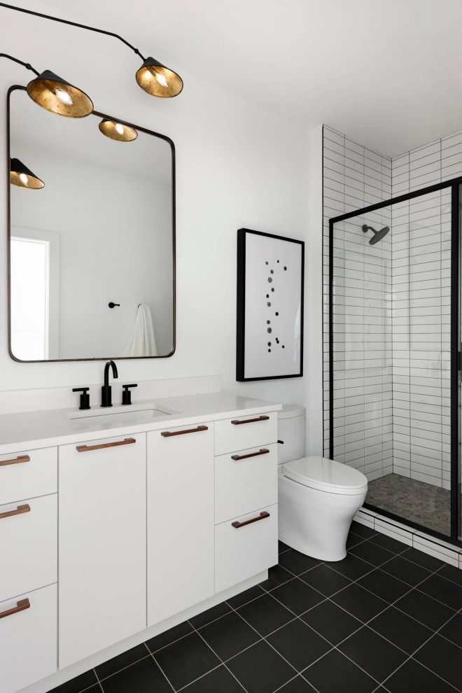 Bild på ett funkis vit vitt badrum med dusch, med vita skåp, vit kakel, vita väggar, svart golv, släta luckor, en toalettstol med separat cisternkåpa, ett undermonterad handfat och dusch med gångjärnsdörr