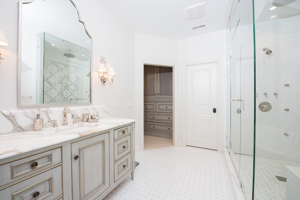 Стильный дизайн: главная ванная комната в классическом стиле с фасадами с утопленной филенкой, искусственно-состаренными фасадами, отдельно стоящей ванной, открытым душем, унитазом-моноблоком, белой плиткой, керамической плиткой, белыми стенами, полом из керамической плитки, врезной раковиной, мраморной столешницей, белым полом и душем с раздвижными дверями - последний тренд