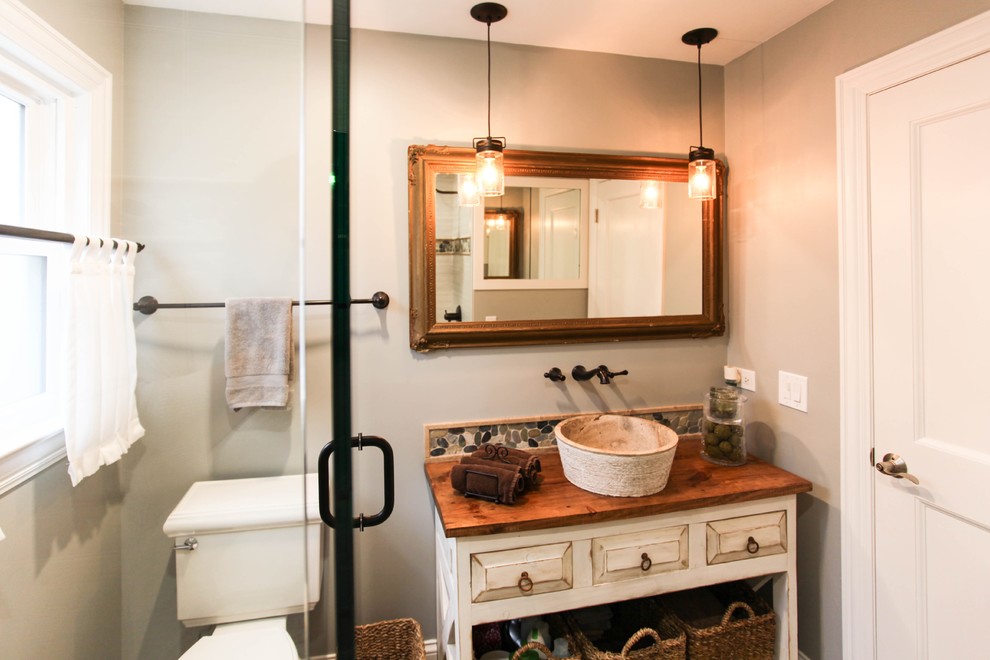 Exempel på ett mellanstort lantligt badrum, med luckor med upphöjd panel, skåp i slitet trä, en dusch i en alkov, en toalettstol med separat cisternkåpa, brun kakel, porslinskakel, grå väggar, klinkergolv i porslin, ett fristående handfat och träbänkskiva