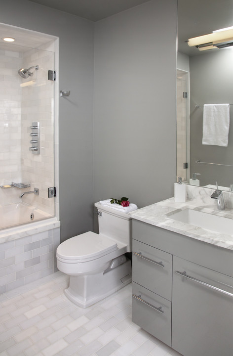 Idéer för att renovera ett mellanstort funkis en-suite badrum, med ett undermonterad handfat, släta luckor, grå skåp, marmorbänkskiva, ett platsbyggt badkar, en dusch/badkar-kombination, en toalettstol med hel cisternkåpa, vit kakel, porslinskakel, grå väggar och klinkergolv i porslin