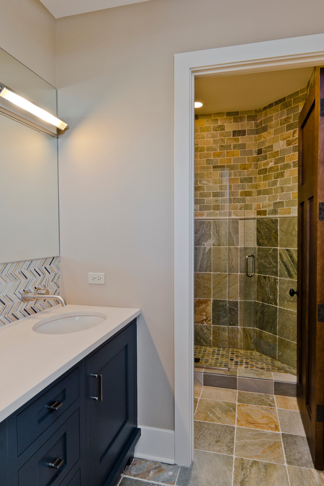 Idéer för att renovera ett mellanstort vintage badrum med dusch, med luckor med infälld panel, blå skåp, en dusch i en alkov, skifferkakel, beige väggar, skiffergolv, ett undermonterad handfat, bänkskiva i akrylsten och dusch med gångjärnsdörr
