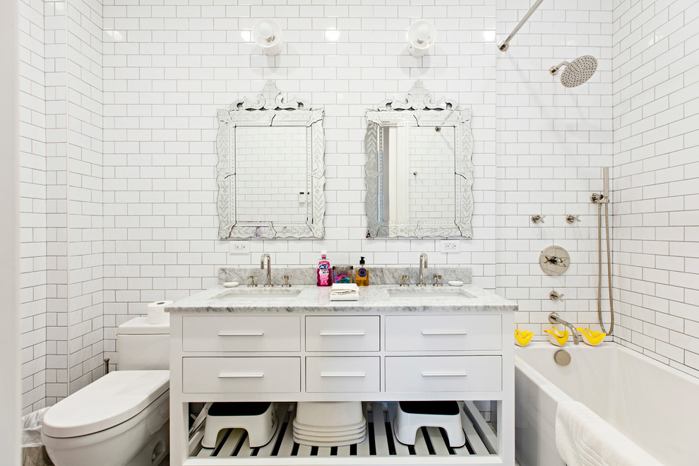 This is an example of a medium sized classic family bathroom in New York with freestanding cabinets, white cabinets, an alcove bath, a shower/bath combination, a one-piece toilet, white tiles, white walls, marble flooring, a submerged sink, marble worktops, metro tiles and white floors.