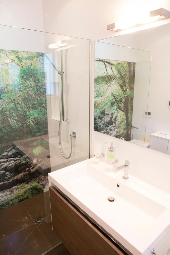 This is an example of a medium sized contemporary family bathroom in Auckland with flat-panel cabinets, medium wood cabinets, a built-in bath, a walk-in shower, a wall mounted toilet, white tiles, ceramic tiles, white walls, ceramic flooring, an integrated sink and solid surface worktops.