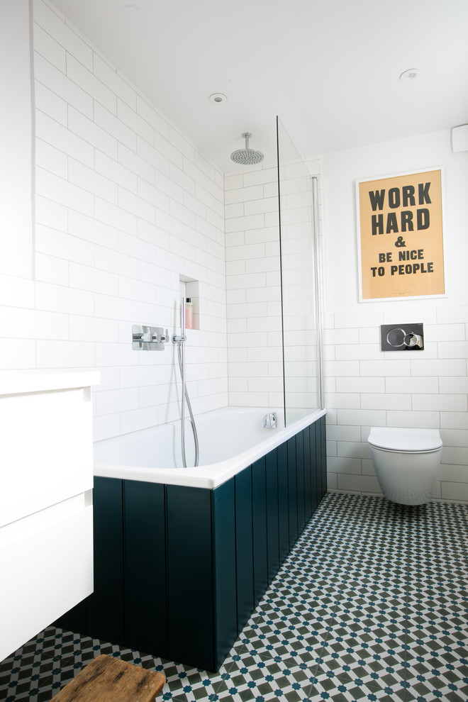 Foto på ett mellanstort funkis badrum, med ett hörnbadkar, en dusch/badkar-kombination, en vägghängd toalettstol, vit kakel, med dusch som är öppen, vita skåp, keramikplattor, vita väggar, klinkergolv i keramik och flerfärgat golv